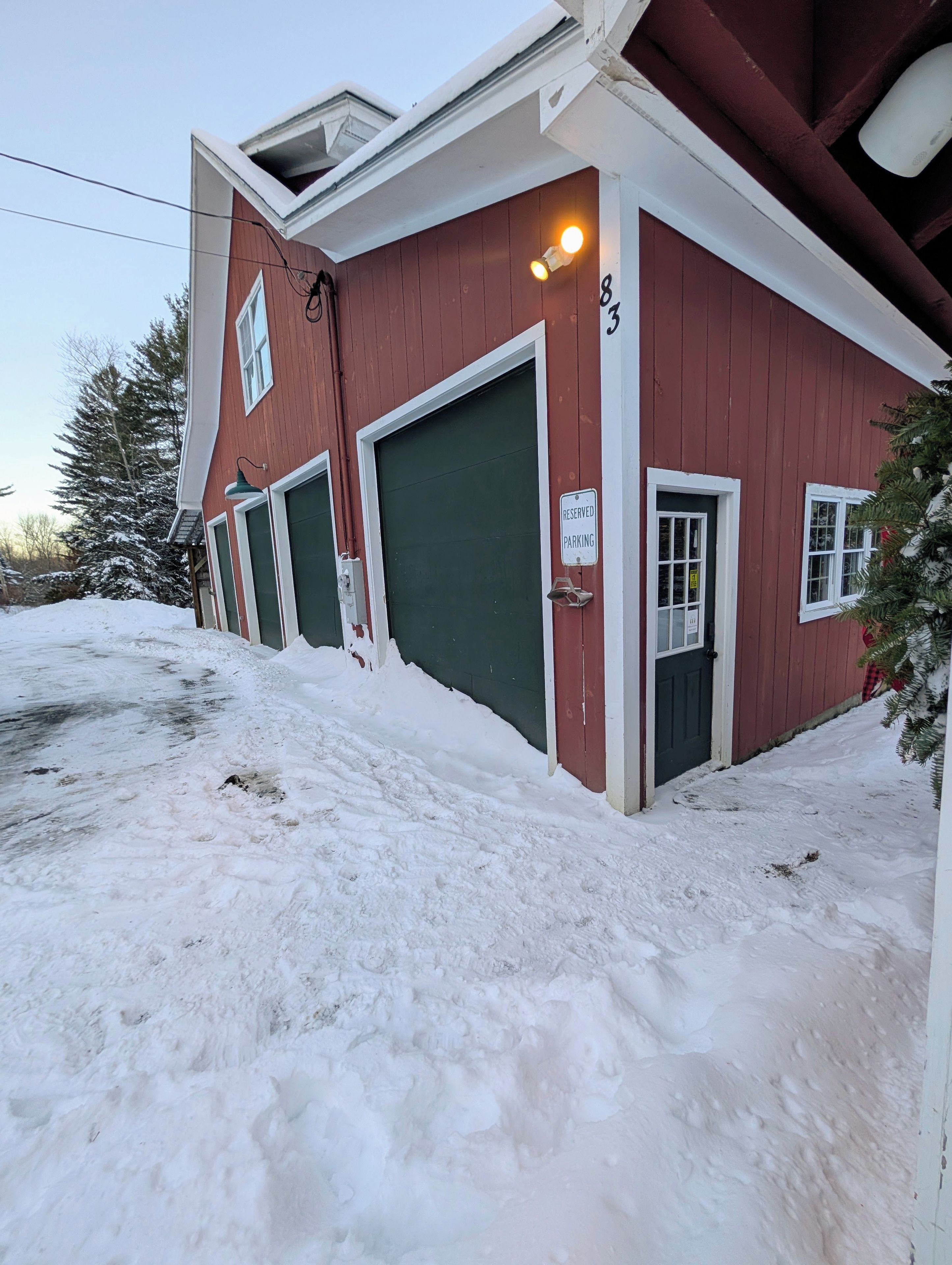 Ein rotes Gebäude mit drei Garagentoren, einem Schild für reservierte Parkplätze und einem mit Schnee bedeckten Boden.