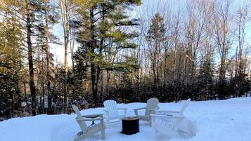 A snow-covered outdoor seating area with Adirondack chairs and a fire pit.