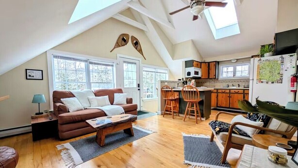 Un loft spacieux avec de hauts plafonds, un salon confortable avec un canapé marron et une table basse, une cuisine avec des meubles en bois et un coin repas avec une table et des chaises.
