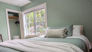 Une chambre avec un lit, une fenêtre avec des stores, un placard et une chaise.