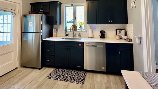 A modern kitchen with dark cabinets, stainless steel appliances, and a patterned rug.