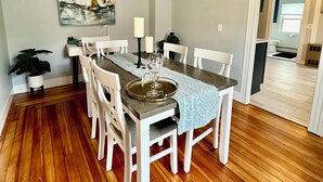 A dining area with a wooden table, white chairs, a chandelier, and a painting on the wall.