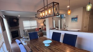 A dining area with a wooden table and blue chairs, a stone fireplace, and a kitchen in the background. - 5 BR - 3 BA <2 Primary BR> SLEEPS 10 - 3 Pools - Linens & Bath Towels Provided (Rehoboth Beach)