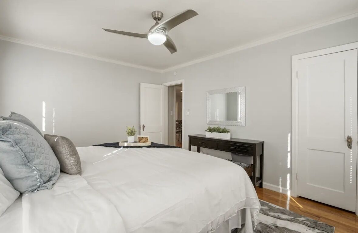 Un dormitorio con cama, ventilador de techo, cómoda, espejo y puerta.