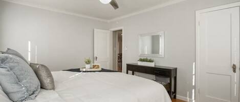 Un dormitorio con cama, ventilador de techo, cómoda, espejo y puerta.