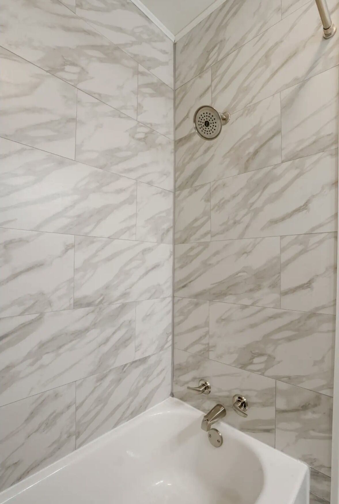 A bathroom with a white bathtub, a showerhead, and marble-patterned walls.