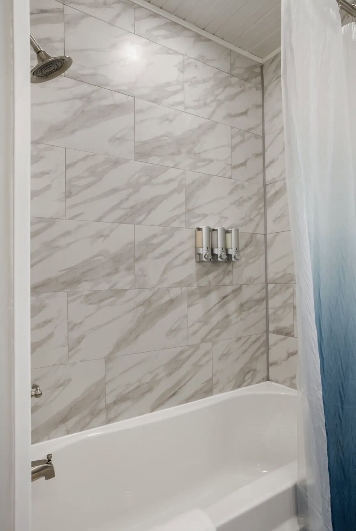A bathroom with a marble tile shower wall, a bathtub, and a showerhead.