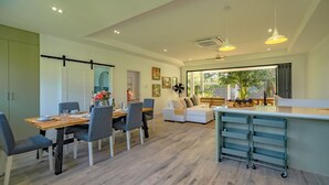 A modern living room with a dining area, large windows, and a kitchen counter. - Escape to Serenity: Your Dreamy 4-BR Mountain View Getaway (Tambon Rawai)
