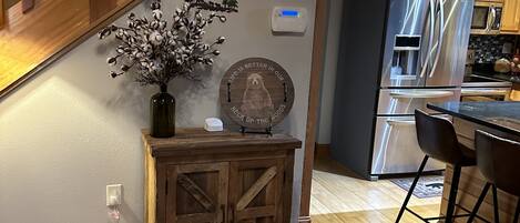 A wooden staircase leading to a kitchen area with a stainless steel refrigerator, wooden cabinets, and a decorative wall piece.