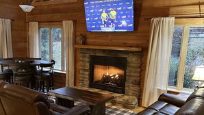 Una sala de estar acogedora con chimenea de piedra, sofás de cuero, una mesa de comedor y un televisor de pantalla plana mostrando un evento deportivo.
