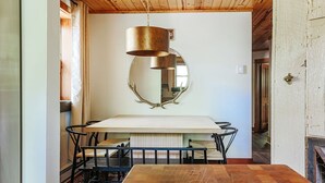 Ein Essbereich mit einem Holztisch, schwarzen Metallstühlen, einer hängenden Messinglampe und einem Wandspiegel mit Geweihorn-Dekorationen.