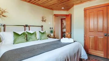 A neatly made bed with a grey blanket and green pillows, a wooden ceiling, and a wooden door.