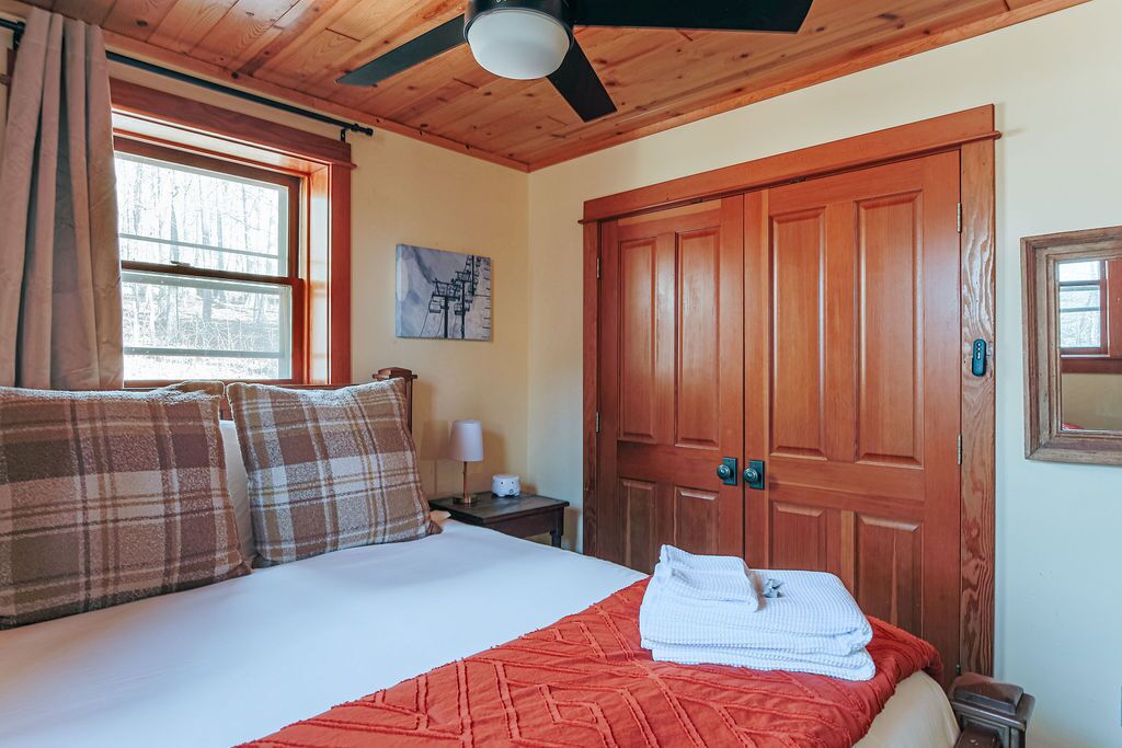 A bedroom with a bed, a wooden door, a nightstand, and a window.