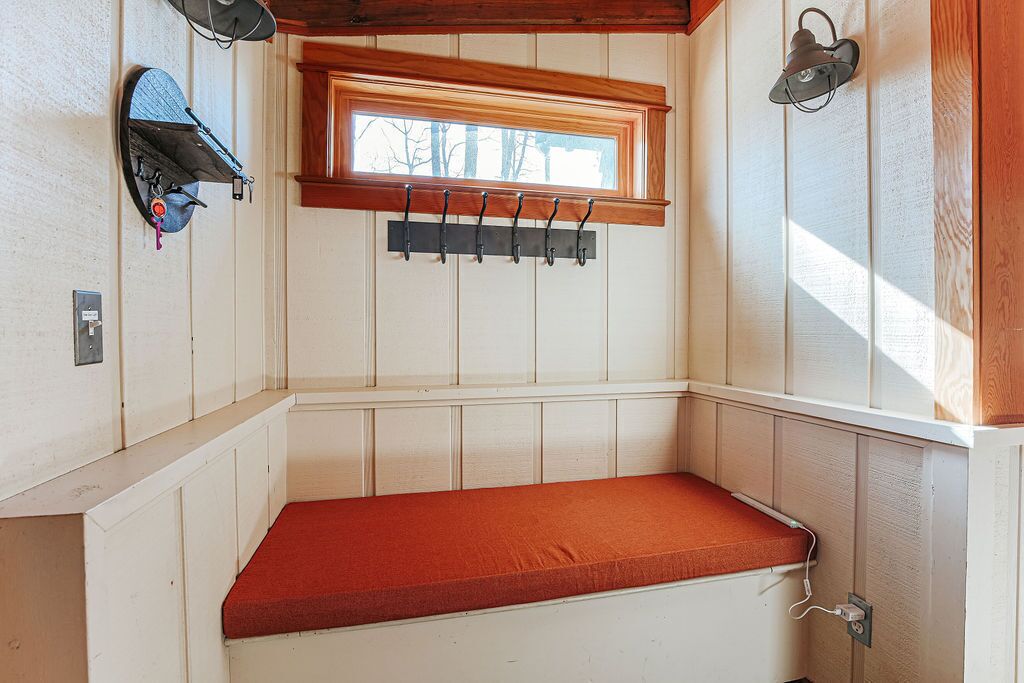 A corner room with a bench, a window, a coat rack, and a wall-mounted lamp.