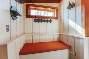 Ein Eckzimmer mit einer Bank, einem Fenster, einem Kleiderständer und einer Wandlampe.