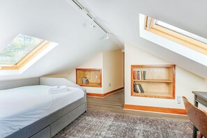 A bedroom with a bed, skylights, a bookshelf, and a desk.
