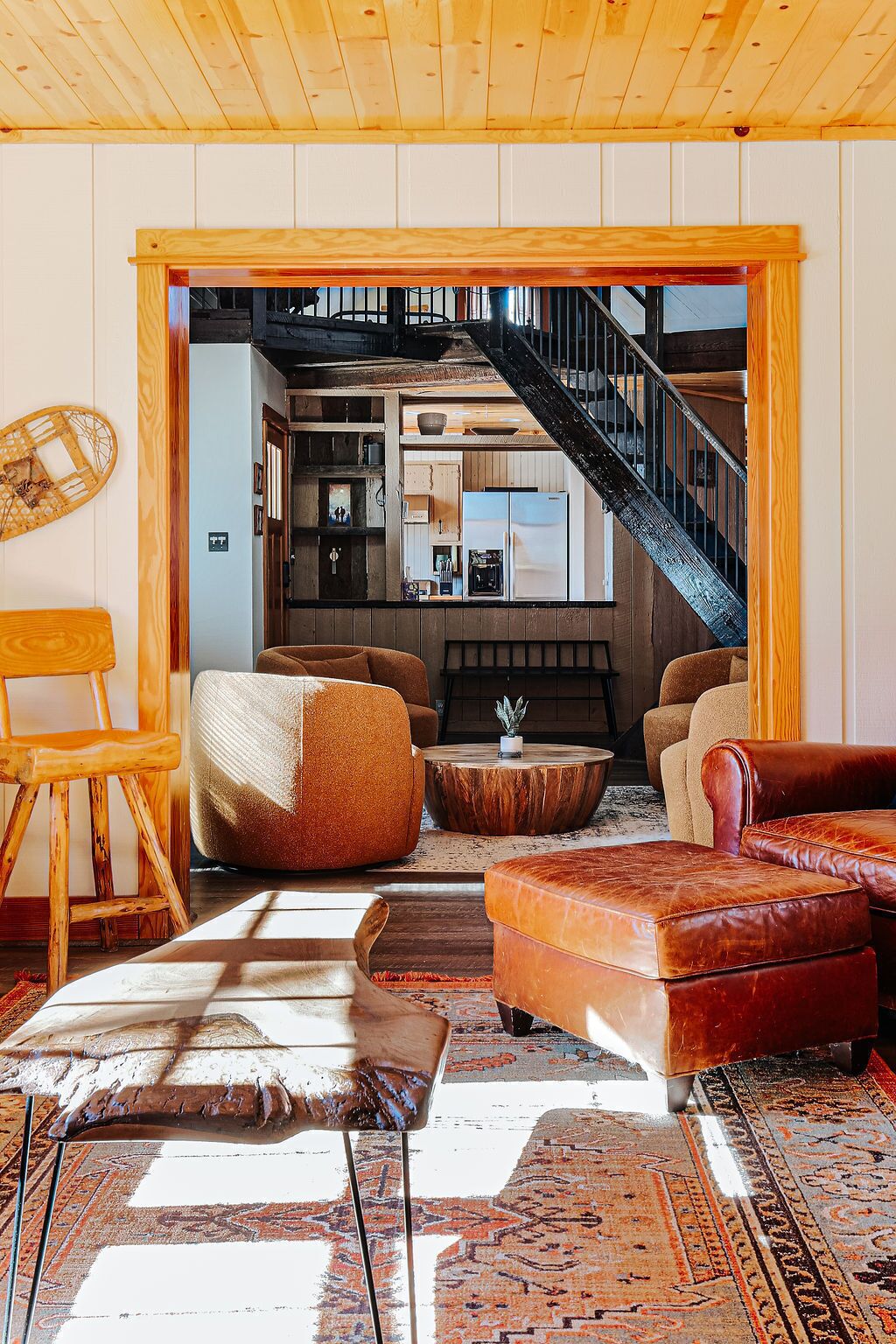 A cozy living room with a wooden ceiling, a staircase leading to an upper level, and a view of a kitchen and dining area.