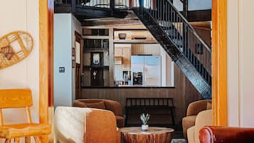 A cozy living room with a wooden ceiling, a staircase leading to an upper level, and a view of a kitchen and dining area.