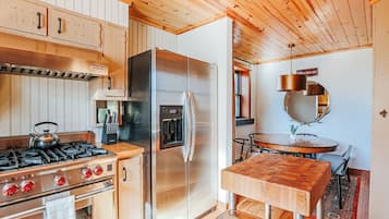A modern kitchen with a stainless steel refrigerator, a gas stove, wooden cabinets, and a wooden dining table.