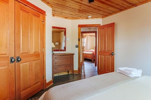 Une chambre avec des portes en bois, une commode, un lit avec du linge de lit blanc et un miroir.