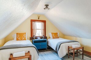 Un dormitorio estilo buhardilla acogedor con dos camas, una ventana con cortinas, una mesita de noche de madera y un ventilador de techo.