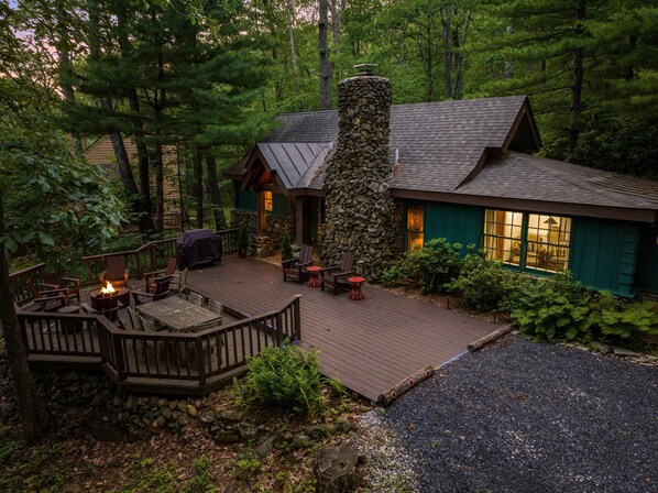 A cabin with a stone chimney, a deck with outdoor seating, and a stone wall.