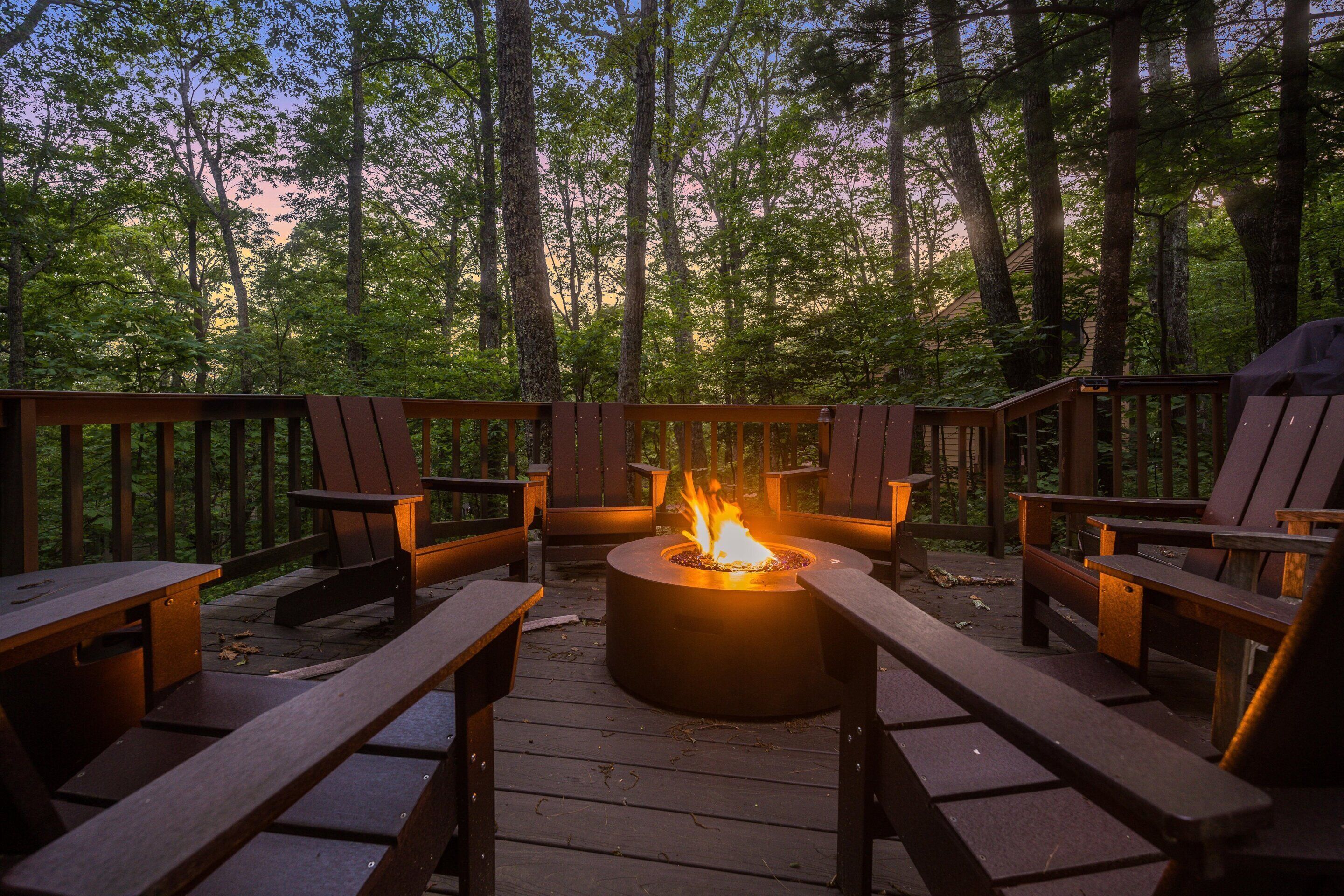 A deck with a fire pit, wooden chairs, and a view of the forest.