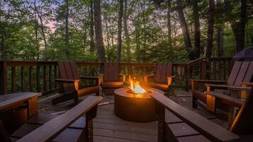 A deck with a fire pit, wooden chairs, and a view of the forest.