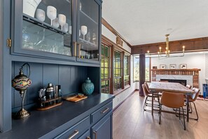 Eine Küche mit einem dunkelblauen Schrank, einem Holztisch und Stühlen. Über dem Tisch hängt eine Chandelier, und das Fenster bietet Blick ins Grüne.
