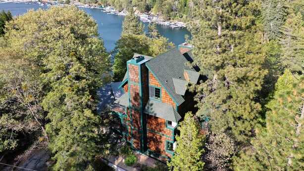 A large house with a steep roof, surrounded by dense forest and a lake with boats. - Lake Reflection Point-Upscale Lake View House! 4 Bed/4.5 Bath! Air Conditioning! (Lake Arrowhead)