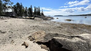 A rocky beach with a wooden structure and trees. - Berry Cottage, private dock, overlooking a sandy b (South Thomaston)