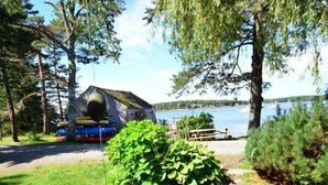 A stone pathway leading to a rustic cabin by a lake, surrounded by greenery and trees. - Berry Cottage, private dock, overlooking a sandy b (South Thomaston)
