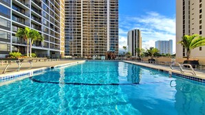 A swimming pool with clear blue water, surrounded by tall buildings and palm trees.