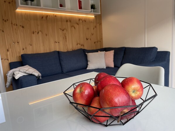 A modern living room with a wooden wall, a blue sofa, and a white table with a wire fruit basket.
