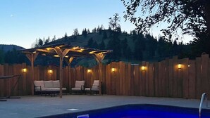 A poolside area with a wooden pergola, seating, and a wooden fence. - Runaway Express Coach (Oliver)