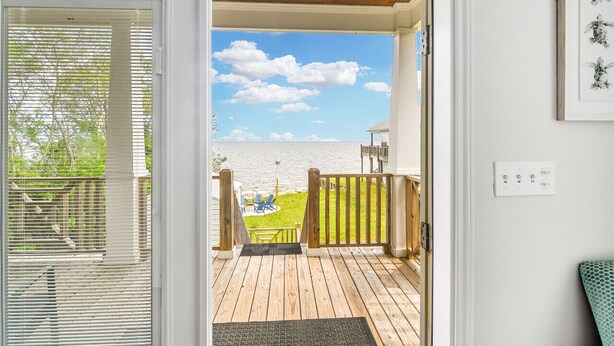 Terraza de madera con vista a un lago y un área verde con sillas.