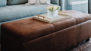 Una sala de estar con sofá, reposapiés y una mesa de centro con un jarrón de flores.