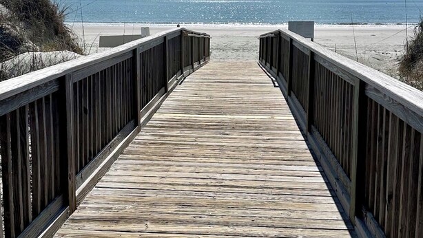 Un paseo marítimo de madera que conduce a una playa con cielo despejado.