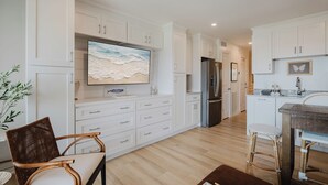 Una cocina moderna con armarios blancos, un televisor de pantalla plana grande y un comedor con sillas de mimbre.