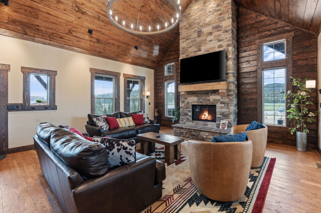 A spacious living room with a stone fireplace, leather furniture, and large windows offering views of the outdoors.
