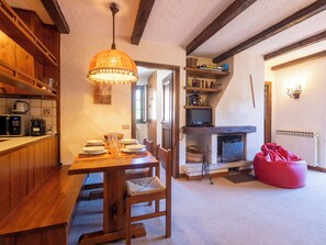 A cozy dining area with a wooden table set for four, a hanging lamp, and a fireplace with a television.