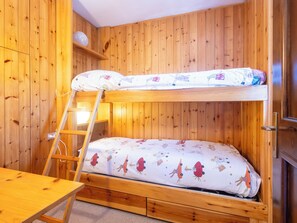 A bunk bed with a ladder, wooden walls, and a small table.