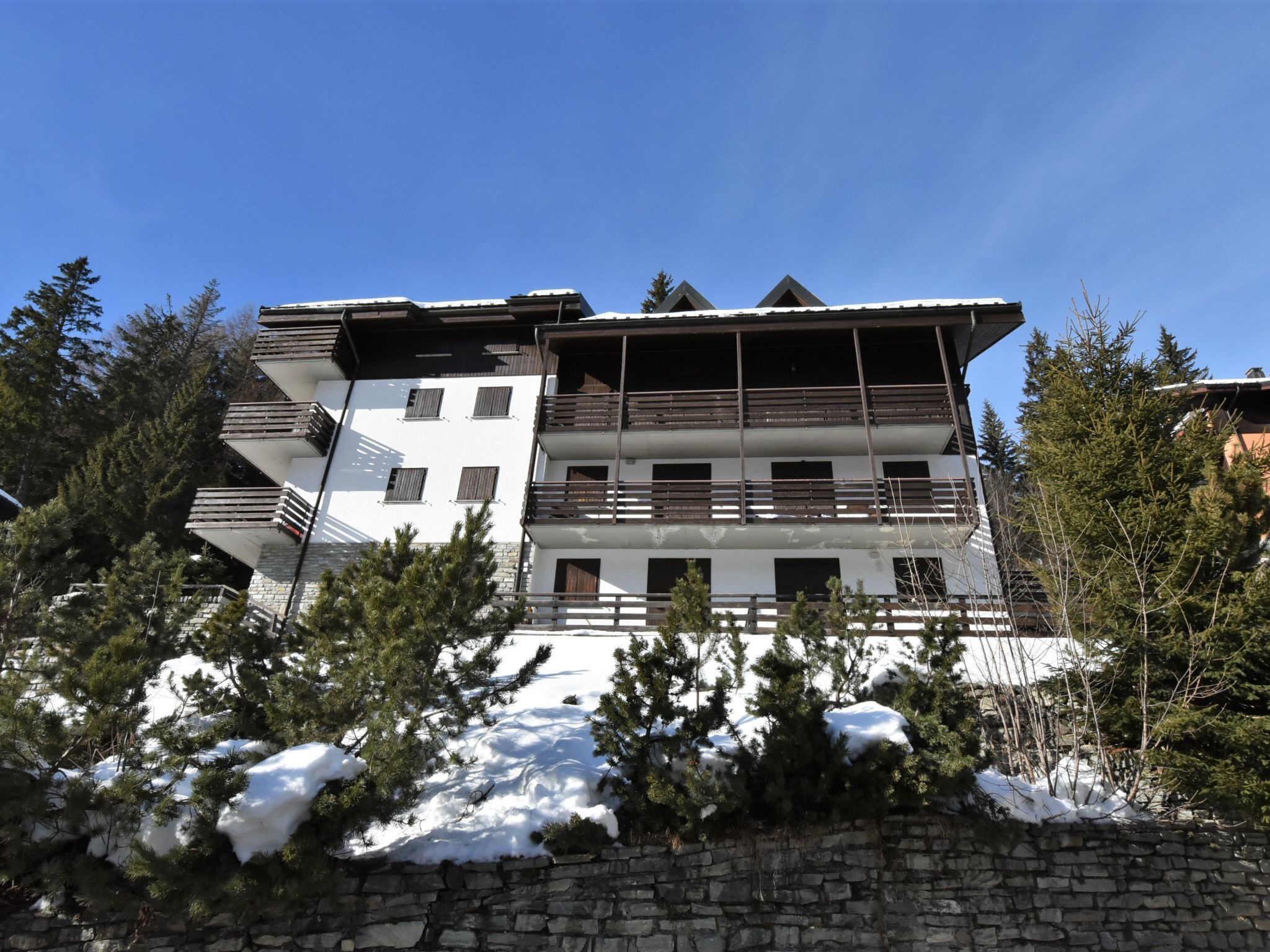 A multi-story building with balconies and a stone wall in front.