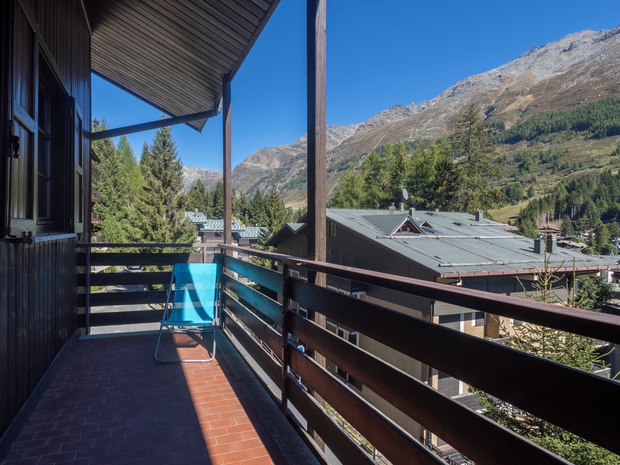 Un balcón con vista a montañas, una silla y un edificio de techo inclinado.
