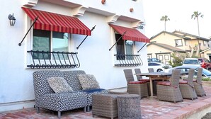 A patio with wicker furniture, red awnings, and a white building with balconies. - Walk to Beach! Entire SC Triplex (San Clemente)