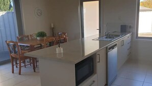 Een kleine keuken met een ingebouwde magnetron, een spoelbak en een eethoek met houten stoelen en een tafel.