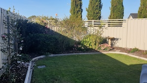 Een goed onderhouden achtertuin met gazon, bloembedden en een houten omheining.