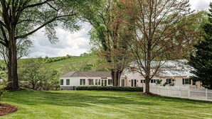 A two-story house with a large lawn, surrounded by mature trees and a white picket fence.