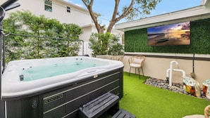 Un jacuzzi con vista a un atardecer, rodeado de vegetación y un televisor montado.