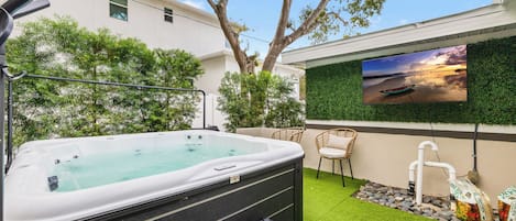 Un jacuzzi con vista a un atardecer, rodeado de vegetación y un televisor montado.